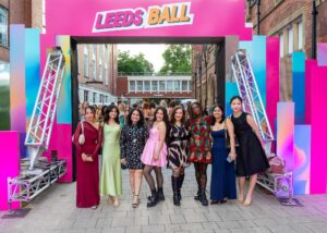Students in ball gowns posing under the Leeds Ball arch